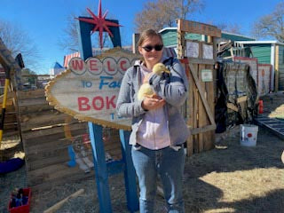 Person holding a duck in front of a colorful sign with 'Welcome to Fabulous Bok Vegas Texas' text.